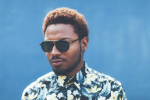 Portrait Of Modern Young Black Man With Sunglasses In Front Blue Background