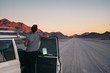 © Micky Wiswedel/Stocksy - Woman on a road trip through the desert leaning out of her car watching a sunset