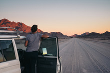 Woman On A Road Trip Through The Desert Leaning Out Of Her Car Watching A Sunset