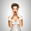 Glamorous surprise / Shocked and surprised pinup bride in a vintage wedding corset on grey background.
