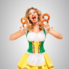 Wall Mural - Emotional waitress / Beautiful Oktoberfest woman wearing a traditional Bavarian dress dirndl holding pretzels, on grey background.