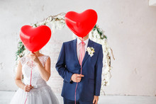 Happy Groom And Bride Covered Their Faces With Red Balloons At Wedding Party Indoors