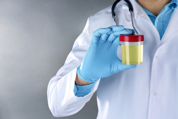 Closeup of doctor holding plastic jar with urine on grey background