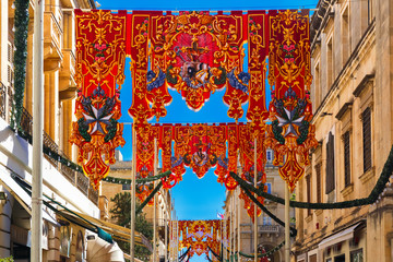 Wall Mural - Festively decorated street with banners for St Augustine Feast in the old town of Valletta, Malta. Flaming, arrow pierced heart - symbol of St Augustine