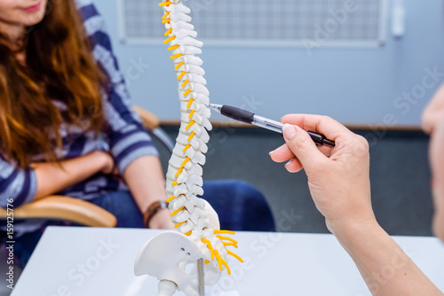 Cuadros en Lienzo Closeup medical doctor woman pointing on spine model and explaining female patient her problem