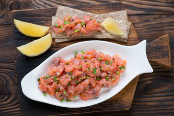 Wall Mural - White plate with salmon tartar in a rustic wooden setting, above view