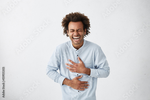 Cuadros en Lienzo Positive and joyful Afro American male with fine crop of hair bursting into laughing holding his hands on stomach can`t stopping laughing after hearing funny anecdote