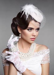 Wall Mural - Fashion Retro elegant woman portrait. Wedding hairstyle. Brunette bride model present white hat, gloves and pearls jewelry accessories over gray studio background.