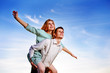 © cezarksv - Young guy piggybacking cheerful girlfriend like airplane on the background of sky