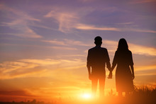 Young Couple Is Holding Hands On A Background Sunset Silhouette