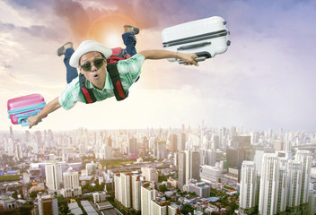 happiness face of asian traveling man flying with two luggage bag floating mid air over town skyscraper