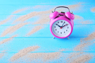 Wall Mural - Pink alarm clock with beach sand on blue wooden table