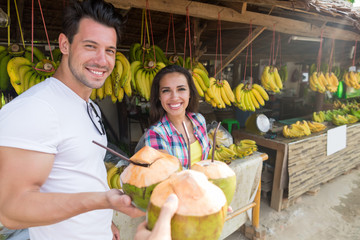 Wall Mural - Couple Drink Coconut Cocktail On Street Traditional Fruits Market, Young Man And Woman Travelers