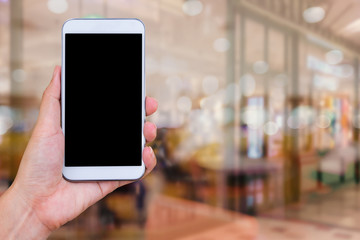 Poster - hand holding white mobile phone with blank black screen on blurred cafe.