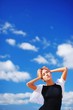 © raisondtre - Woman standing outdoors with eyes closed and arms outstretched against the blue sky and beautiful scenic clouds