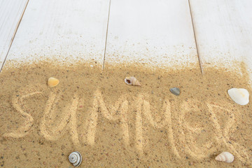 Wall Mural - Word 'summer' writing on sand with shells over white wooden background