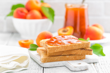 Wall Mural - Toasts of bread with apricot jam and fresh fruit with leaves on white wooden table. Tasty breakfast.