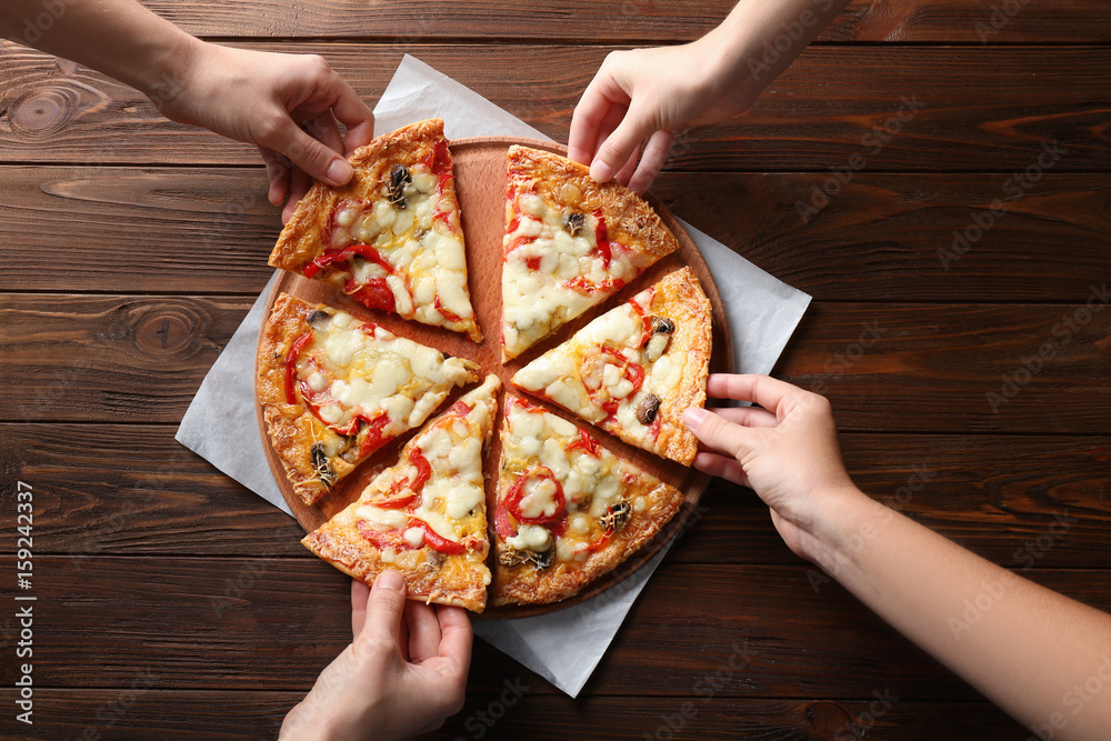Female hands taking pizza slices on wooden table