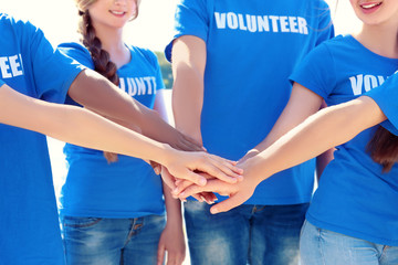 Canvas Print - Young people putting hands together outdoors. Volunteer concept