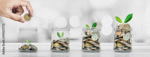 Fotografía Hand putting coin in glass bottles with plants glowing, Saving money and investm