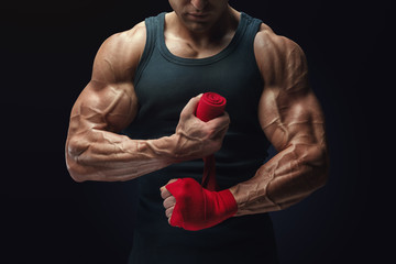 Close-up photo of strong man wrap hands on black background Man is wrapping hands with red boxing wraps isolated on black background Strong hands and fist, ready for training and active exercise