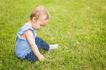 Wall Mural - Fourteen months old baby girl sitting in the shadow on the grass on the sunny summer day