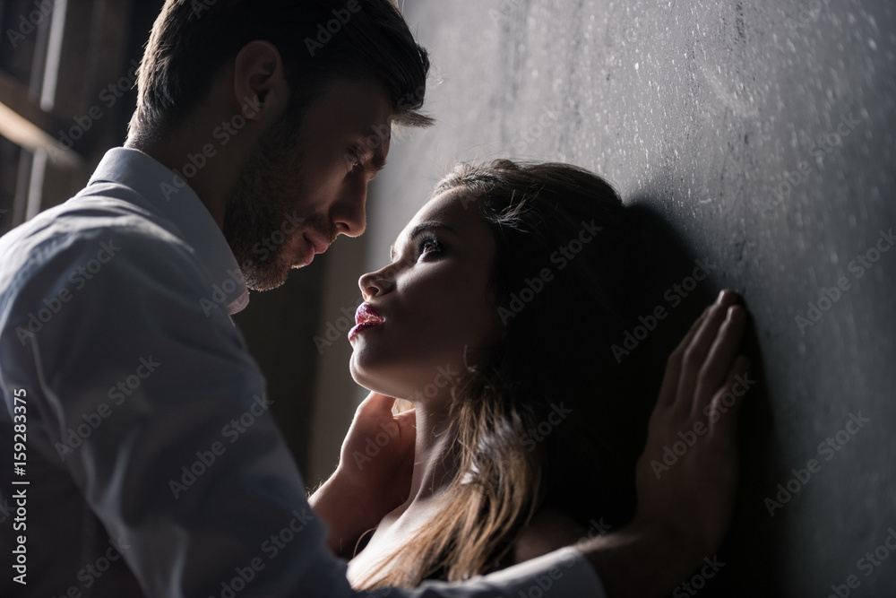 young passionate couple able to kiss while standing near the wall - obrazy, fototapety, plakaty 