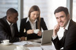 © fizkes - Cheerful businessman wearing suit looking at camera sitting at desk with international partners, experienced team leader holding business meeting for subordinates at background, consulting services