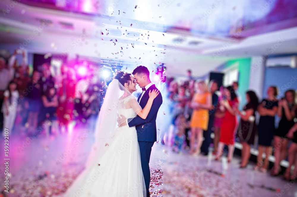 Touching and emotional first dance of the couple on their wedding with confetti and colorful lights on the background. - obrazy, fototapety, plakaty 