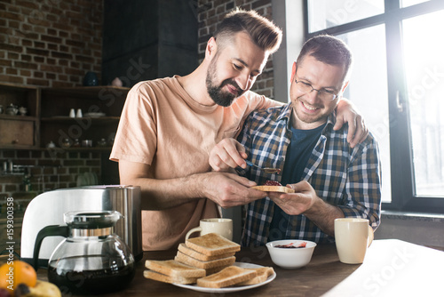 Happy homosexual couple preparing toasts with jam for breakfast at home Fototapet