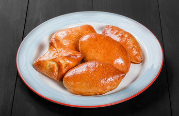 Wall Mural - Fresh bread buns pies patties in plate on black wooden background. Bakery products. Hot and healthy breakfast, top view, flat lay