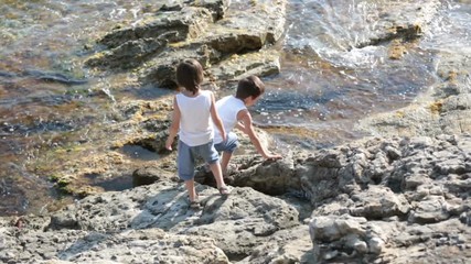 Canvas Print - Two children, boys, running on rocks on the shore of the sea, having fun