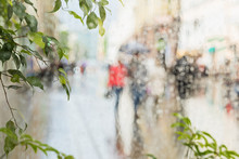 Raindrops On Window Glass, Few Unrecognizable People Rush Home Under Umbrellas, Abstract Blurred Background. Concept Of Seasons, Weather, Modern City.