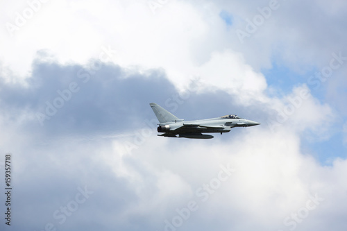 Plakat Myśliwiec odrzutowy latający niski przeciw błękitnemu i chmurnemu niebu.
