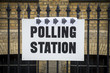 British election polling station sign hanging on classic wrought iron fence in front of yellow brick wall in London, UK