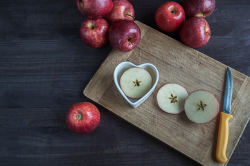 Red apples on the table, a cutting board, a heart-shaped dish and a sliced apple. Harvest, a lot of apples. Fruits, antioxidants, vitamins.