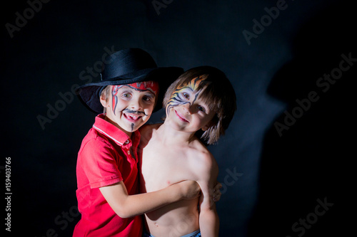 Fototapeta na szkło Two children, brothers, painted as tiger and pirate, playing together in studio