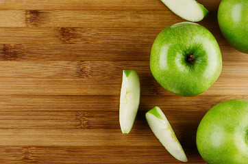 Wall Mural - Green apples with slices on bamboo brown plank, top view, copy space.