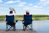 Fototapeta Uliczki - Couple of people resting on chairs in front of the lake
