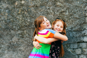 Two funny girl friends playing outdoors, wearing dresses