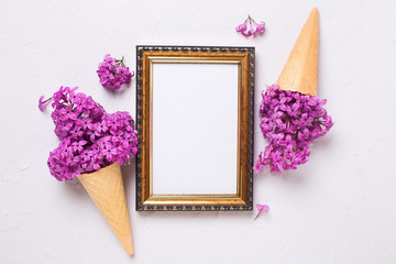  Fresh lilac flowers in waffle cones and empty  golden frame for text on grey textured background.