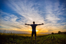 Man standing in an open field at sunset with open arms - embracing nature