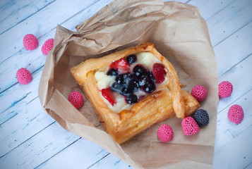 Wall Mural - Pastry with red berries on paper, isolated on a blue wooden background. Summer fruit dessert.