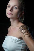 Blond Woman With Henna Tattoo On Her Shoulder Looking At The Camera Over Black Background