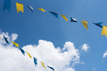 Blue And Yellow Bunting Flags On String Waving In Wind At Funfair Festival Against Blue Summer Sky