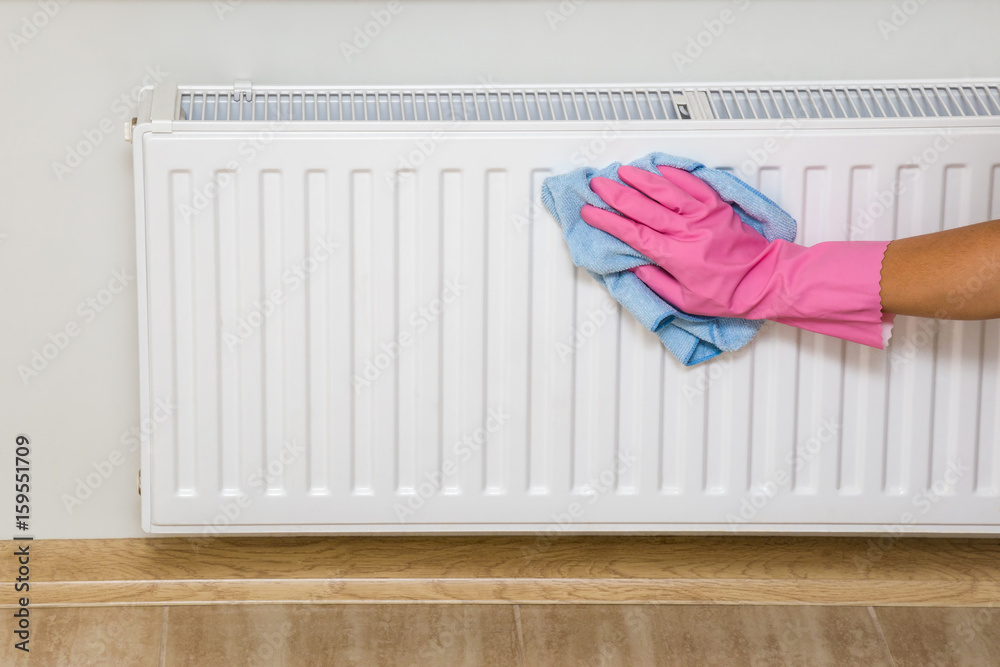 Hand in pink rubber protective glove with rag wiping a heater radiator. Early spring cleaning or regular clean up. Maid cleans house.