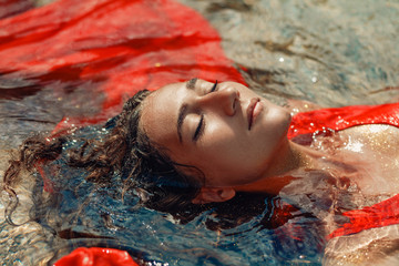 Wall Mural - beautiful young woman in red dress laying dowm in water