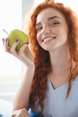 Sticker - Cheerful redhead lady sitting at the table indoors eating apple