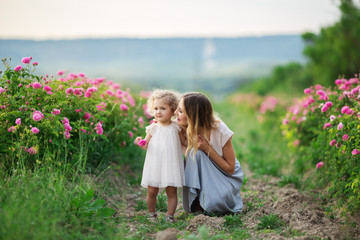 Beautiful young child girl with mother are wearing casual clothes sitting in a garden with pink blossom roses