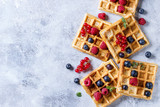 Fototapeta  - Homemade square belgian waffles with fresh ripe berries blueberry, raspberry, red currant over gray texture background. Top view with space